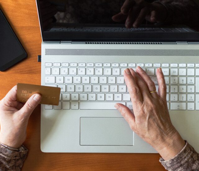 A senior holding their debit card while typing their information into a computer