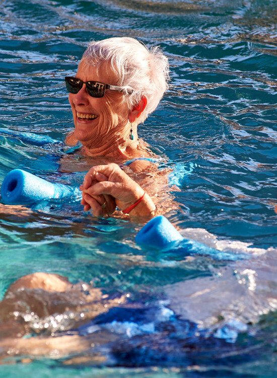 Two seniors in a pool swimming with a pool noodle