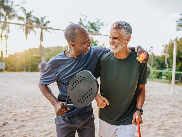 Two senior friends playing beat tennis on sand tennis court