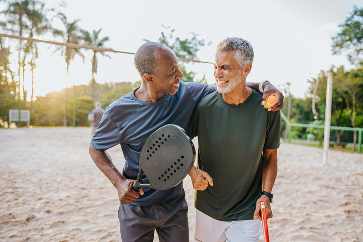 Two senior friends playing beat tennis on sand tennis court