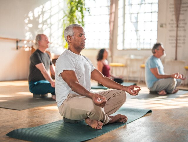 A diverse group of happy retirees in comfortable workout clothes participating in a yoga class led by a young instructor. The seniors are happily stretching and performing yoga poses, and meditation emphasizing the importance of fitness and well-being in later life.