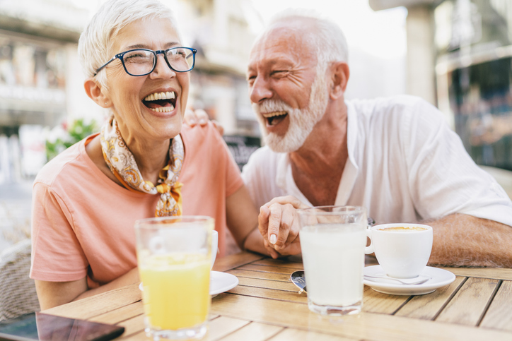 Older couple enjoying a laugh and a drink outside in the sun.